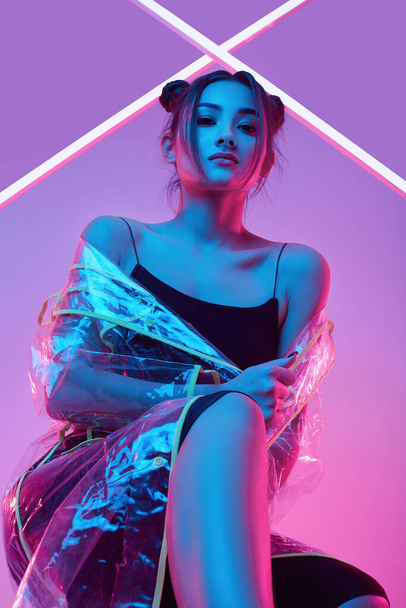 Retrato de mulher asiática bonita elegante em uma capa de chuva na moda em torno de luzes coloridas brilhantes neon uv posando em estúdio
 - Foto, Imagem