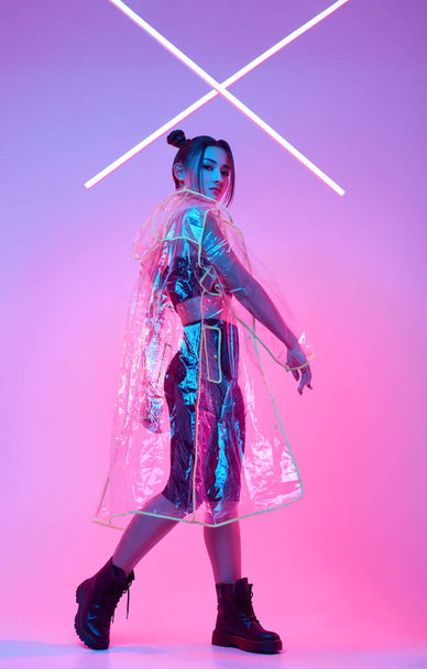Portrait of elegant beautiful Asian woman in a fashionable raincoat around colourful bright neon uv lights posing in studio - Фото, зображення