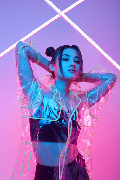 Portret eleganckiej pięknej Azjatki w modnym płaszczu przeciwdeszczowym wokół kolorowych jasnych neonów uv świateł pozowanie w studio - Zdjęcie, obraz