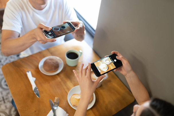 Vista superior de una joven pareja tomando fotos de su comida para las redes sociales en un restaurante
 - Foto, imagen