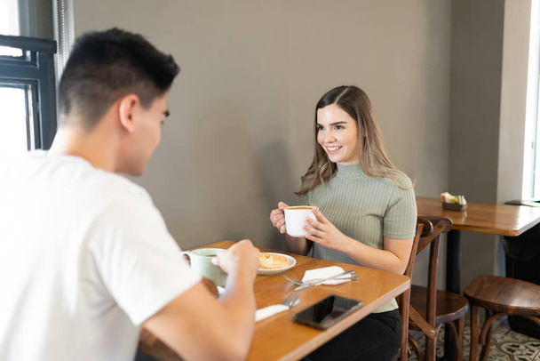 Güzel genç bir kadın ve erkek arkadaşı bir pastanede kahve ve hamur işi yiyorlar. - Fotoğraf, Görsel