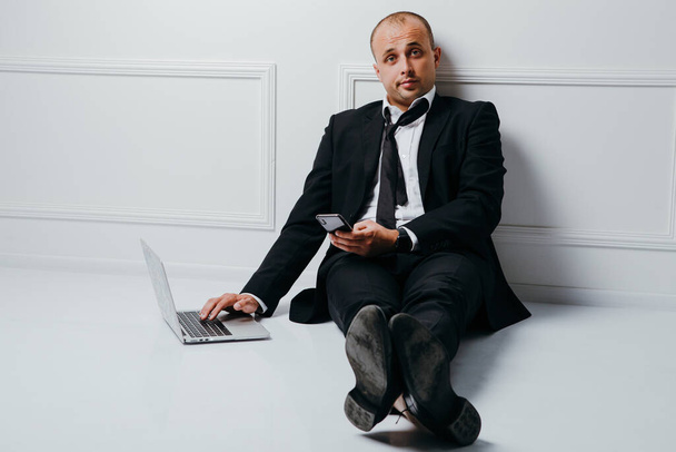 Молодой бизнесмен сидит на полу и работает на ноутбуке
 - Фото, изображение