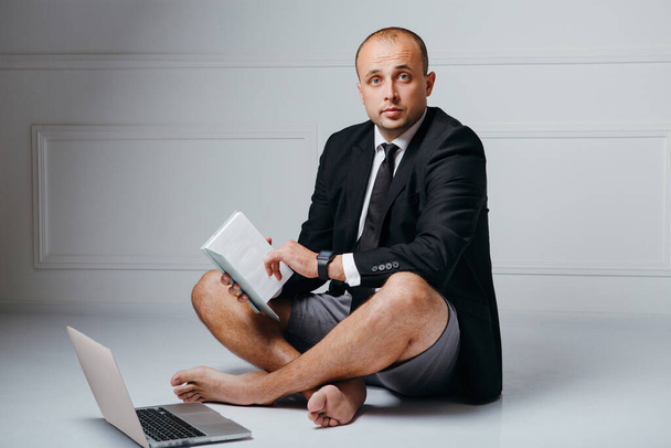Biznesmen siedzi na podłodze z notatnikiem i laptopem w biurze - Zdjęcie, obraz
