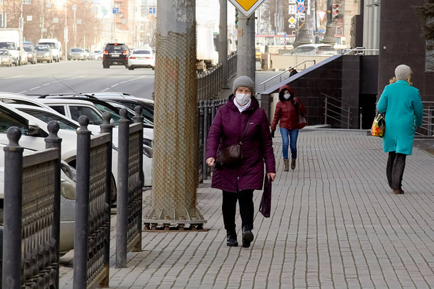 MOSCOW, RUSSIA - APRIL, 2020. An adult woman with a respirator on her face from the COVID-19 virus is walking down the street in the city during the daytime. Outerwear, spring. Quarantine. Restriction on the movement of people in public places - Foto, afbeelding