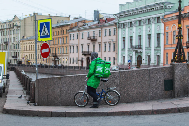 Saint-petersburg, Russia - 31 March 2020: Courier in a branded green jacket and mask, delivering orders by bike around the city - Fotoğraf, Görsel