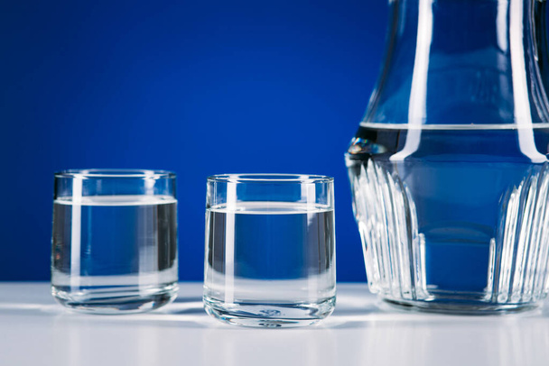 Glass jug of water and two glasses isolated on blue background - Photo, Image