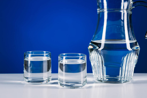 Lasi kannu vettä ja kaksi lasia eristetty sinisellä pohjalla
 - Valokuva, kuva