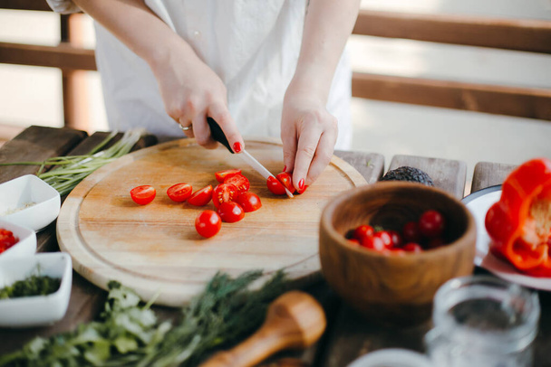Woman's hands cutting cherry tomatoes on a wooden plate. Making guacamole - 写真・画像