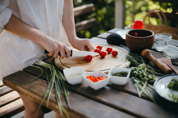 Woman's hands cutting cherry tomatoes on a wooden plate. Making guacamole - Foto, Bild
