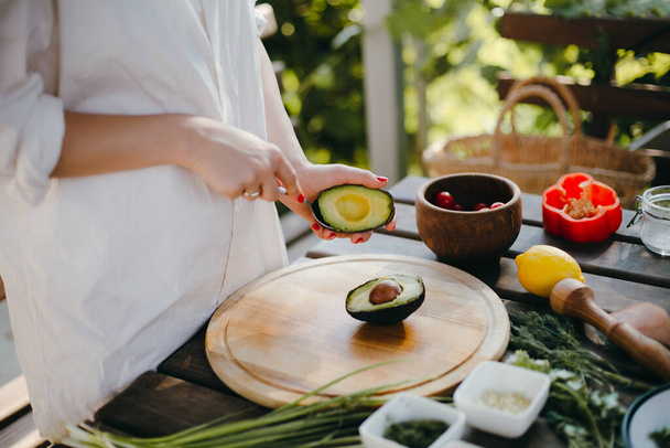 Manos de mujer pelando aguacate para guacamole con una cuchara. Cocina de picnic afuera
 - Foto, Imagen