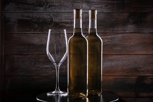 Két fehér borosüveg egy üres pohárral az asztalon, fa háttérrel - Fotó, kép