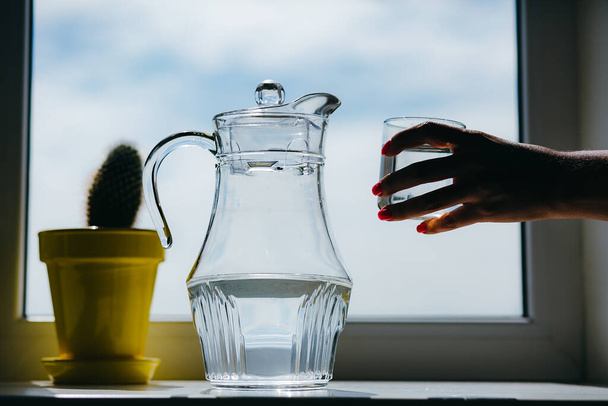 Mano della donna che tiene un bicchiere d'acqua su un davanzale della finestra
 - Foto, immagini