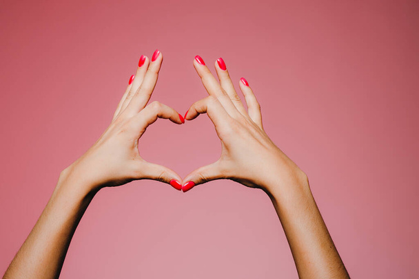 Las manos de la mujer con manicura brillante aislado sobre fondo rosa amor firmar los dedos hacia arriba
 - Foto, imagen