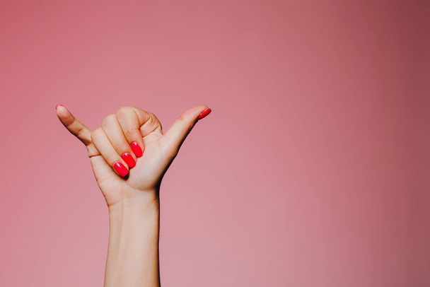 Ręce kobiety z jasnym manicure odizolowany na różowym tle zadzwoń do mnie znak - Zdjęcie, obraz