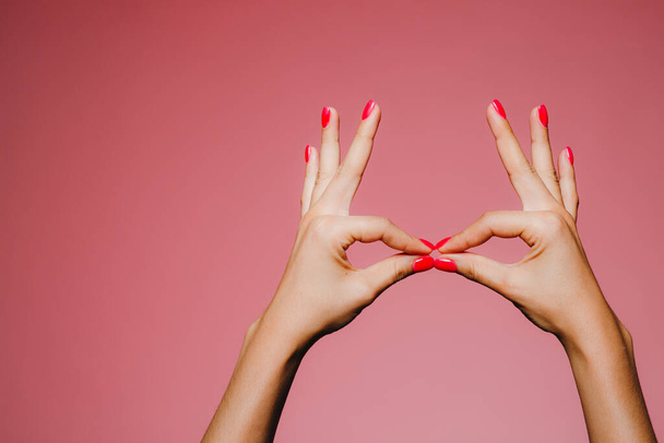 Жіночі руки з яскравим манікюром ізольовані на рожевому фоні цілуючий жест
 - Фото, зображення