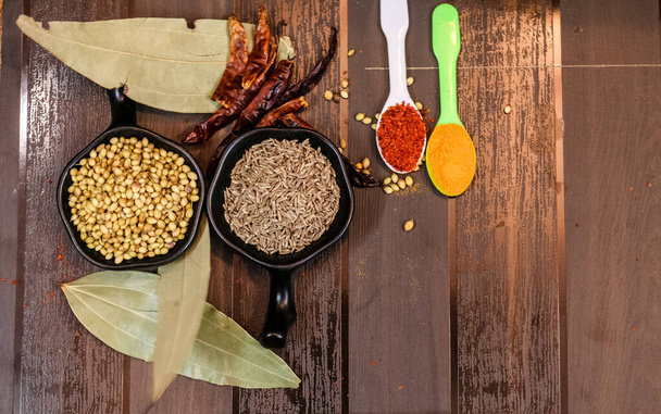 Spezie indiane ed erbe aromatiche su cucchiaio e ciotola con sfondo in legno
 - Foto, immagini