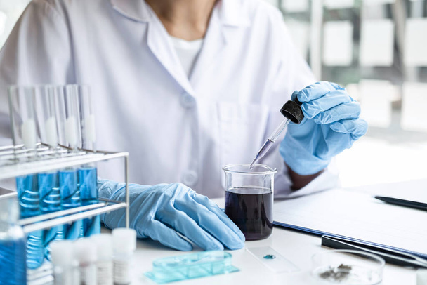 Scientist or medical in lab coat holding dropper with reagent, mixing reagents in glass flask, glassware containing chemical liquid, laboratory research and testing of Microscope. - Photo, image