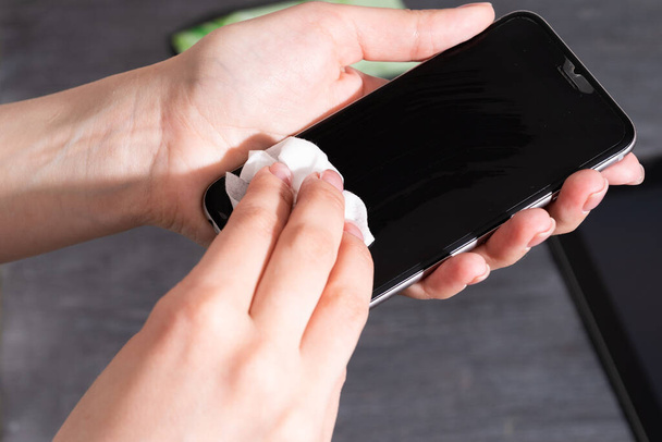 Woman wipes smartphone with a disinfectant - Safety concept during the coronavirus epidemic covid-19 - Photo, Image