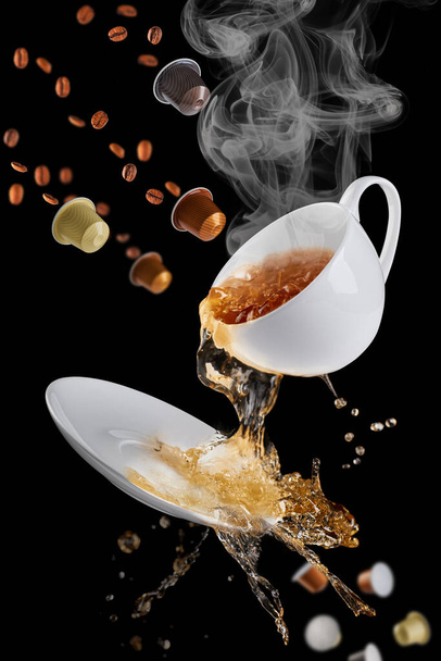 Coffee from the mug spills onto the saucer, splatters of coffee flying in different directions. Coffee capsules approach from above, and used coffee capsules fall from below. - Foto, imagen