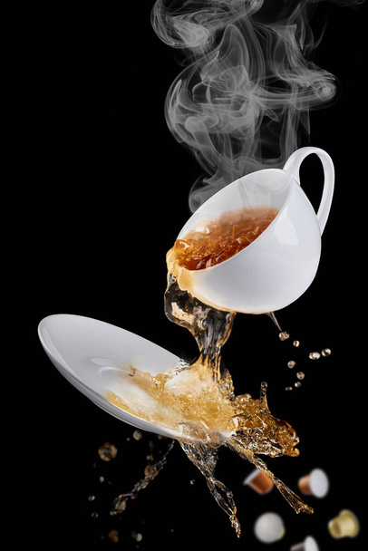 The coffee from the mug splashes out on the saucer, splashes of coffee flying in different directions. Used coffee capsules fall down. - Fotó, kép