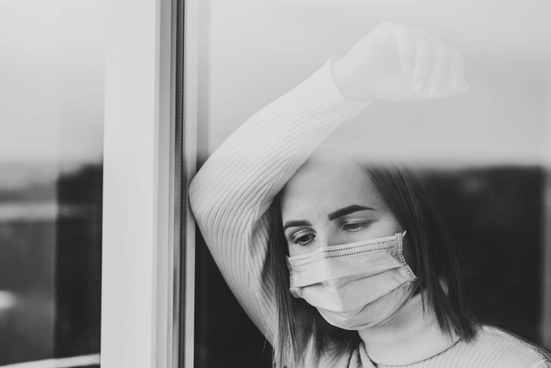 Coronavirus. Sick woman wearing protection face mask looking through the window. Patient isolated in house to prevent infection. Quarantine room at hospital. Black and white photo. - Fotó, kép