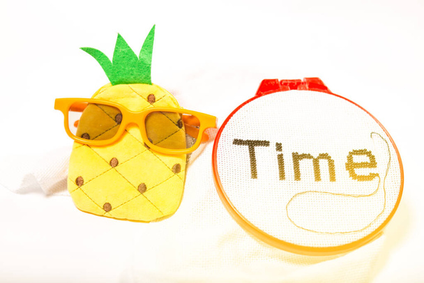 Een pluche ananas met het woord tijd geborduurd met kralen, symboliseert de tijd doorgebracht met uw favoriete eten en voor uw favoriete tijdverdrijf. - Foto, afbeelding