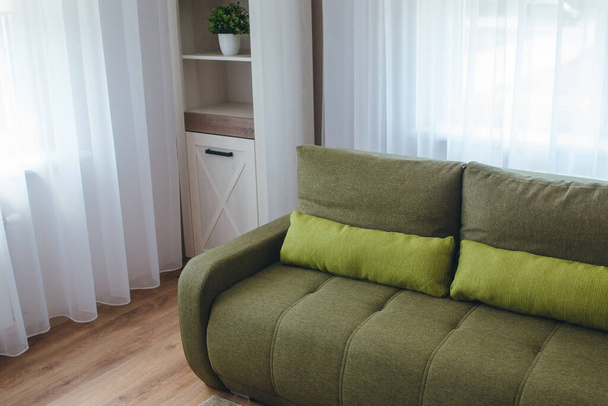 Intern uitzicht op een moderne woonkamer met houten vloer, groene bank en witte boekenplank. - Foto, afbeelding