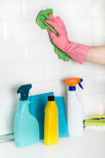 Man cleaning a wall of white subway tiles with a sponge cloth in a close up view - Foto, imagen