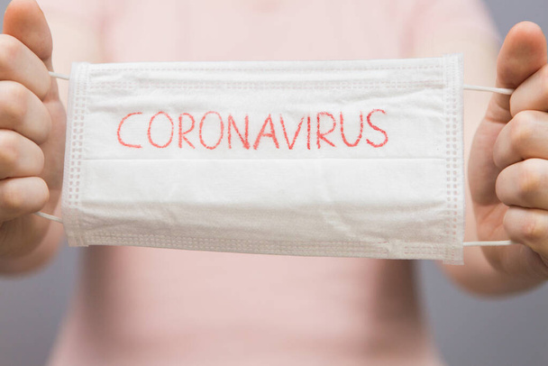 Novel coronavirus - Surgical mask protective mask with CORONAVIRUS text. Chinese coronavirus outbreak. Mask in hands woman - Foto, immagini