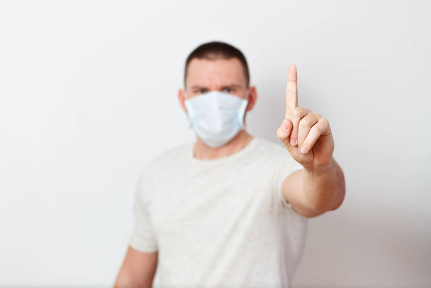 a serious man in a medical mask shows his index finger on a white background - Foto, imagen