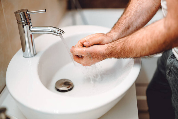 Young male adult washing hands at home using disinfectant and soap, tap water and cleaning cosmetics - Foto, Imagem