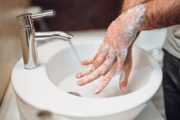 Man carefully washing hands with soap and sanitiser in home bathroom. Coronavirus prevention by washing hands with tap water and soap - Foto, Imagem