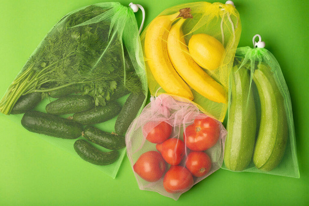Doğal oganik salatalıklar, domatesler, muzlar ve kabaklar yeniden kullanılabilir şeffaf torba, yeşil arka planda üst manzara. Çevre dostu sıfır atık alışverişi. - Fotoğraf, Görsel