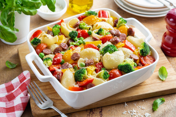 baked vegetable and sausages lumaconi pasta in white baking dish, wooden background, selective focus - 写真・画像