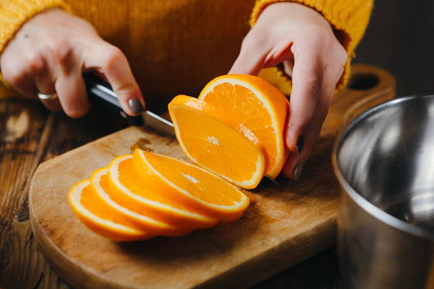 Großaufnahme von Frauenhänden, die Orangen für Glühwein schneiden. - Foto, Bild