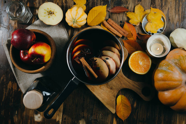 Mulled wine hot drink with citrus, apple and spices in aluminum pot on wooden background. Autumn mood with pumpkins, candles and leaves. - Photo, Image