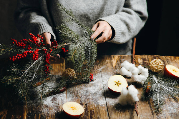 Closeup on table where woman in grey sweater is making Christmas decorations. Wreath making process. - Photo, Image