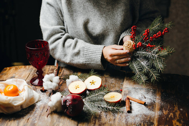 Szekrény az asztalon, ahol a szürke pulóveres nő karácsonyi dekorációkat készít.. - Fotó, kép