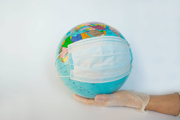 Earth globe dressed in the protective mask on a man's hand in a protective glove. Symbol that people all over planet are quarantined due to the epidemic and pandemic of Coronavirus. White background. - Zdjęcie, obraz