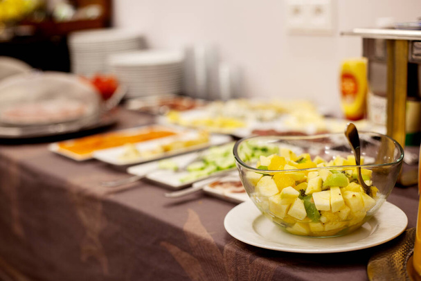 Auf dem Buffettisch steht ein bunter Obstsalat in einem durchsichtigen Glasteller. Gesunder Nachtisch, gesunder Lebensstil - Foto, Bild