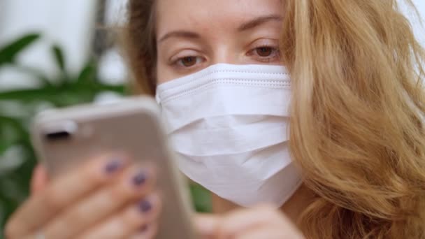 Young Woman wearing white protective mask reads a news on a smartphone - Materiaali, video