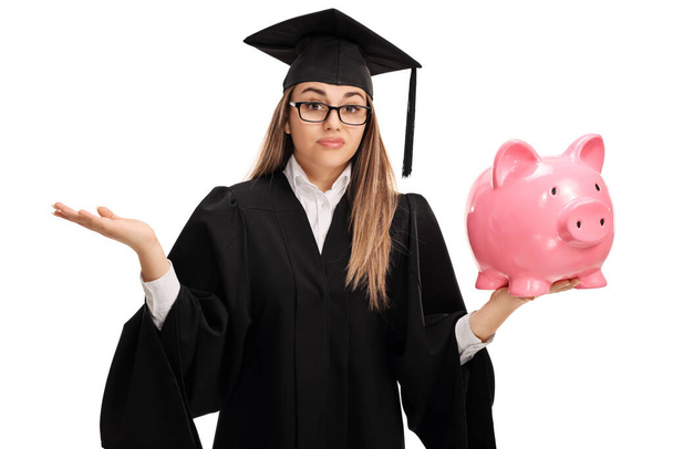 Confused female graduate holding a piggy bank isolated on white background - Foto, Imagem