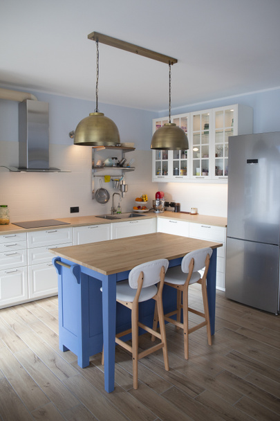 White, bright kitchen with blue island and double brass pendant lights. Vertical shot. - Фото, изображение