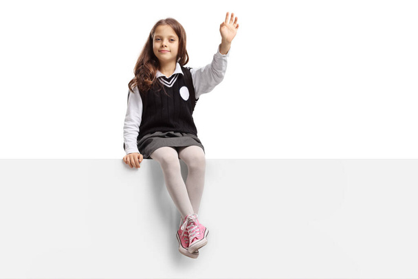 Little schoolgirl sitting on a panel and waving isolated on white background - Valokuva, kuva