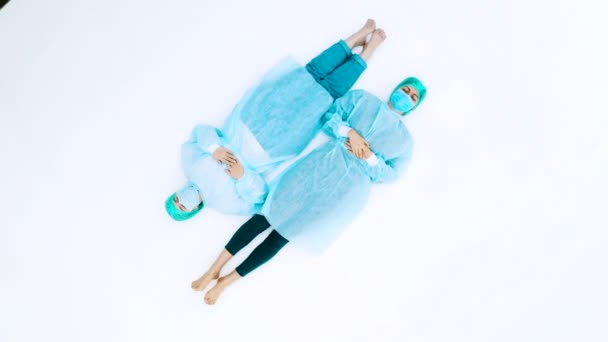 Две женщины в защитных медицинских костюмах и масках для лица. Молодые девушки лежат на белом полу в защитных медицинских пальто, шапках и масках. Трагедия пандемии гриппа
 - Кадры, видео