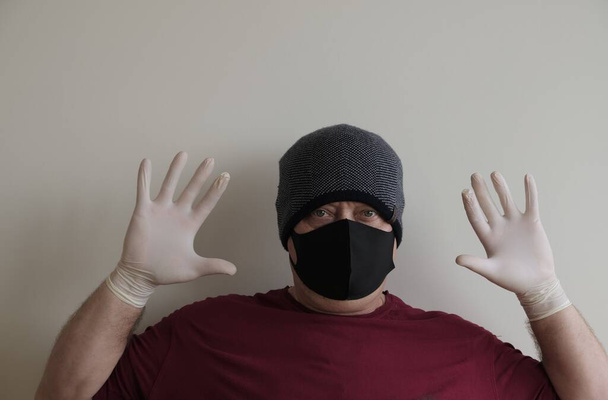 Portret mężczyzny chronionego przed koronawirusem. Białe, lateksowe rękawiczki. Ochrona dłoni przed zakażeniami, wirusami, zarazkami. Izolacja skóry. Na twarzy jest tkaninowa maska. Okulary na oczach.  - Zdjęcie, obraz
