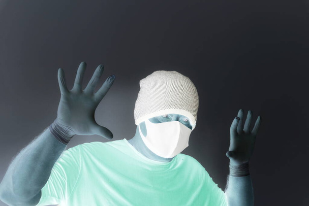 コロナウイルスから保護された男の肖像画。白いラテックスの手袋。感染症、ウイルス、細菌に対する手の保護。皮膚の分離。顔にはファブリックマスクです。目には眼鏡.  - 写真・画像