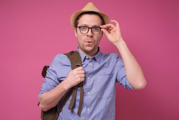 Hombre guapo en sombrero de verano ajustando gafas que parecen interesados en las noticias. Estudio filmado en la pared rosa. Concepto de vacaciones y descanso
. - Foto, imagen