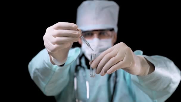 cientista em um laboratório close-up deixa cair uma solução médica em um tubo de ensaio. no fundo preto
. - Filmagem, Vídeo