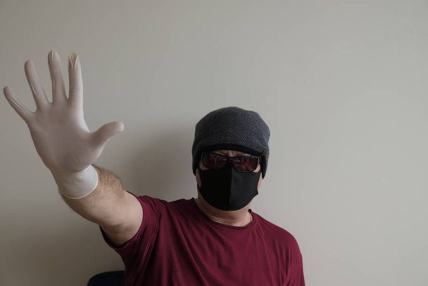 Retrato de un hombre protegido del coronavirus. Guantes blancos de látex. Protección de las manos contra infecciones, virus, gérmenes. Aislamiento de la piel. En la cara hay una máscara de tela. Gafas en los ojos
.  - Foto, imagen